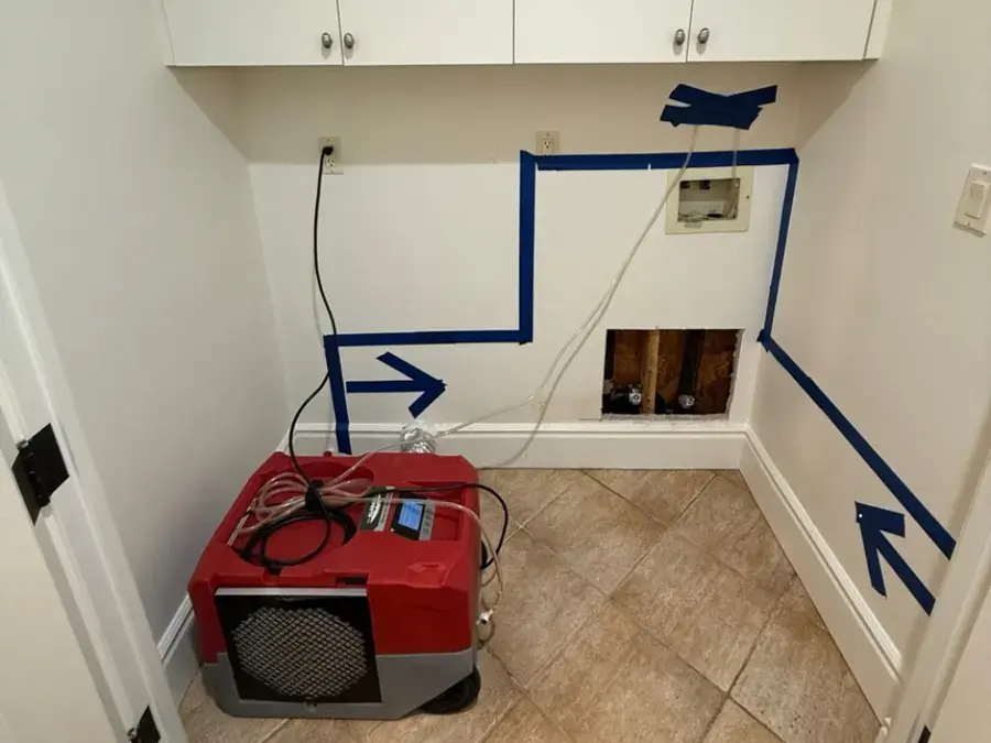 Blue tape marking the mapped wet area on a laundry wall with a dehumidifier drying it in Woodland Hills
