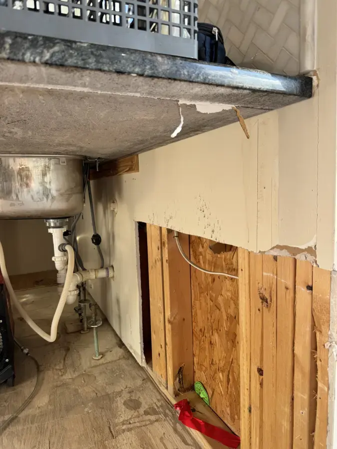 Sink cabinet and lower wall opened to dry framing after water damage in Woodland Hills
