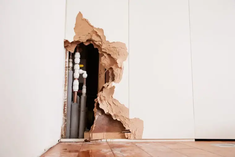 Drywall opened around supply pipes after a burst pipe, with water on the floor