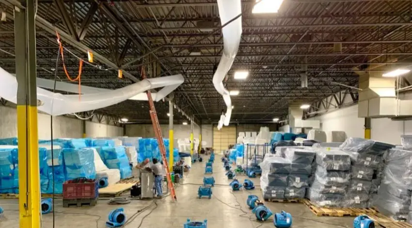 Rows of air movers drying a large commercial warehouse floor after water damage